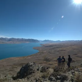 Three hikers standing at a panoramic lookout on Mount Hay with views across Lake Tekapo and distant peaks