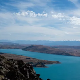 Scenic view over Lake Tekapo from the Mount Hay hiking trail with rocky cliffs in the foreground