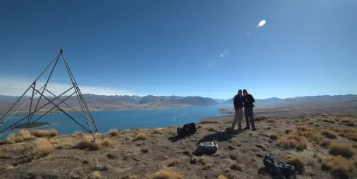 Two hikers posing for a photo near the trig station at the summit of Mount Hay with Lake Tekapo in the background