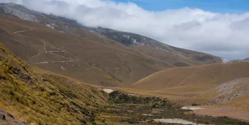 Winding trail leading up the slopes of Mount Ardmore near Lake Tekapo with clouds rolling over the ridge