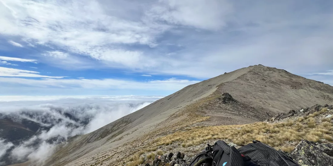 Backpack resting on a rocky alpine slope with Mount Edward’s summit trail rising ahead near Lake Tekapo