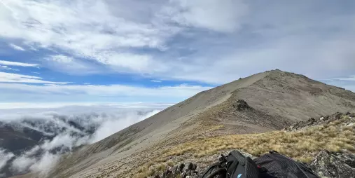 Backpack resting on a rocky alpine slope with Mount Edward’s summit trail rising ahead near Lake Tekapo