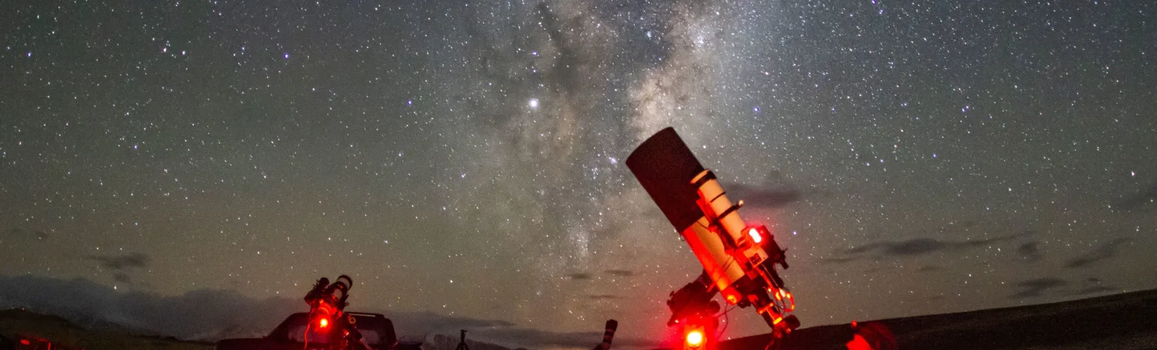 Telescopes glowing red under the Milky Way during an astrophotography night at Lake Tekapo