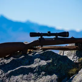 Scoped hunting rifle resting on a rock with mountain scenery in the background near Lake Tekapo