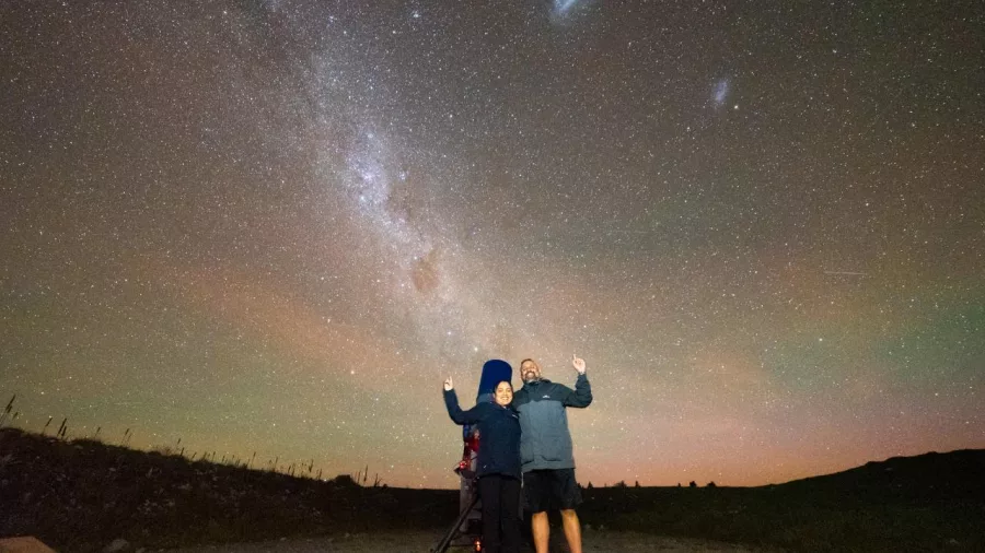 Couple posing under the Milky Way with telescopes during a guided stargazing tour near Twizel