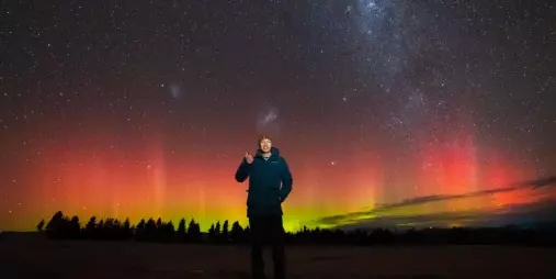 Guest standing beneath a vivid Aurora Australis display during a stargazing tour in Twizel