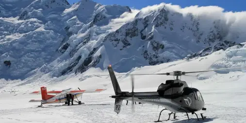 Ski plane and helicopter parked on the Tasman Glacier with towering ice cliffs in the background during the Ultimate Alpine Experience