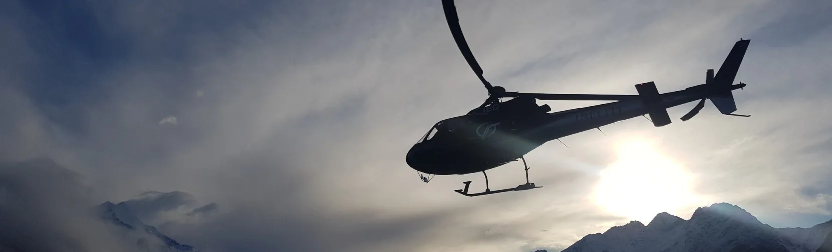 Silhouetted helicopter lifting off at sunset with dramatic mountain backdrop