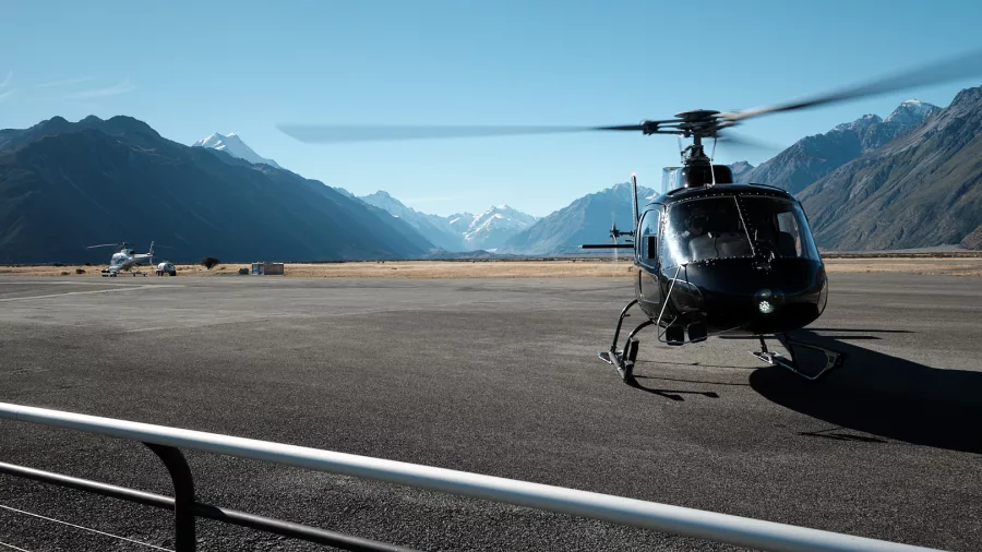 Black helicopter parked at Mount Cook Airport with Southern Alps in the distance