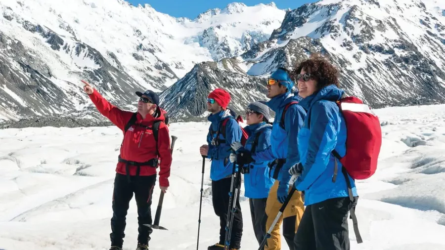 Heli-hiking group on the Tasman Glacier being briefed by a guide as a helicopter approaches