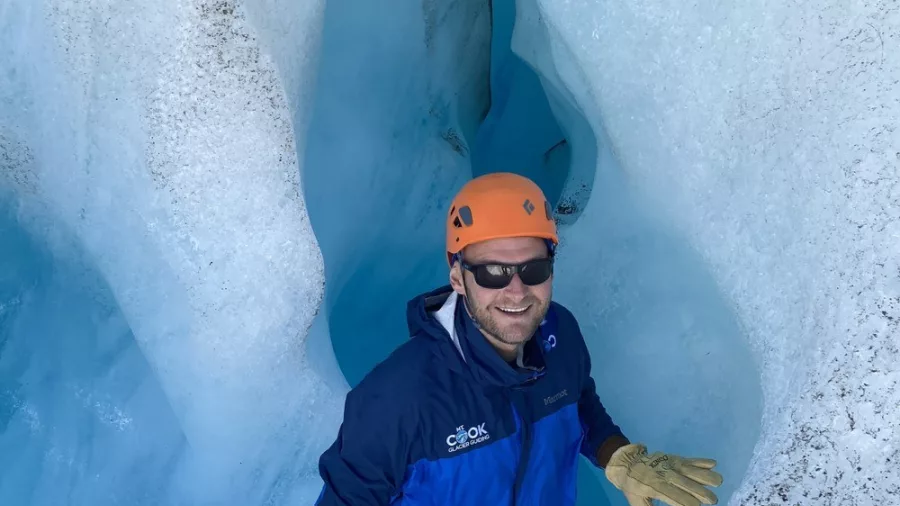 Smiling climber exploring a deep blue ice crevasse on Tasman Glacier, New Zealand.