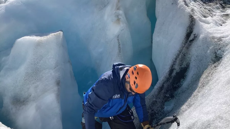 Ice climber navigating a technical wall above a deep crevasse on Tasman Glacier.