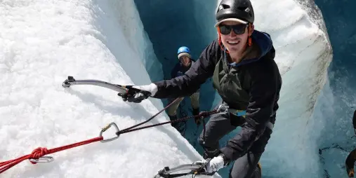 Group of climbers using ropes and ice tools on a bright glacier wall in Mount Cook National Park.