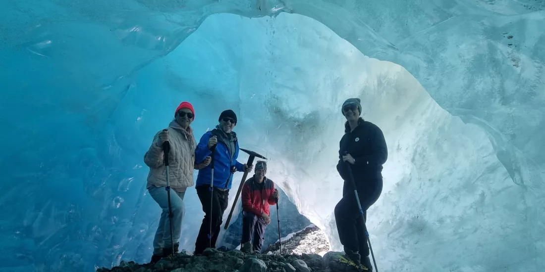 Group of hikers inside a glowing blue ice cave on the Tasman Glacier.