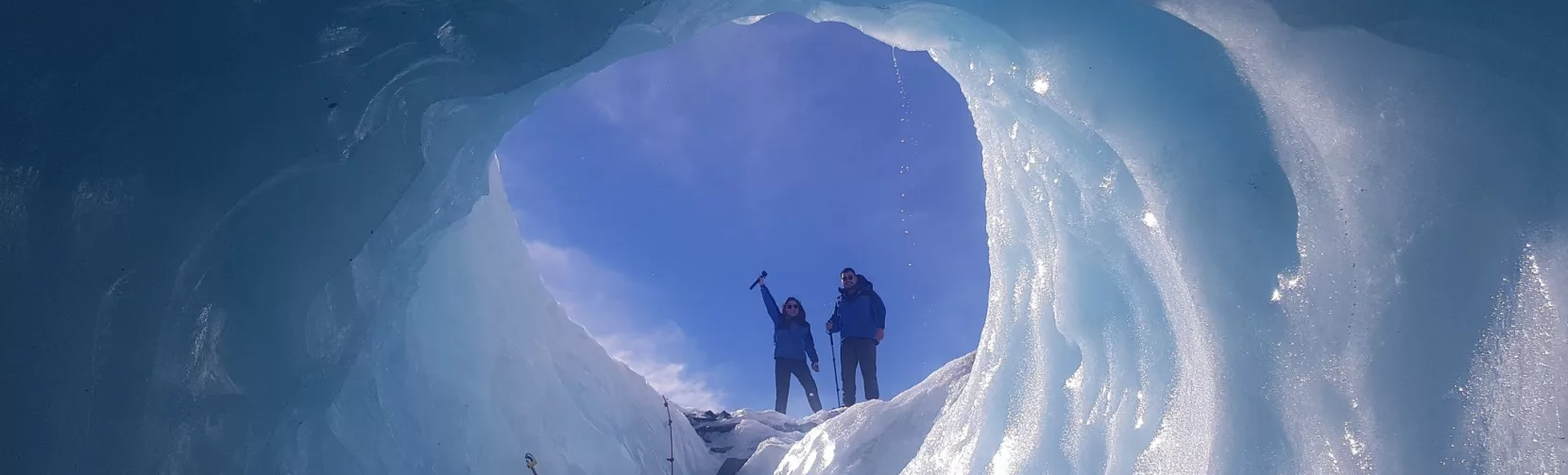Two hikers emerging from an ice cave on Tasman Glacier, seen from inside the tunnel.