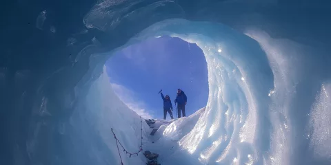 Two hikers emerging from an ice cave on Tasman Glacier, seen from inside the tunnel.