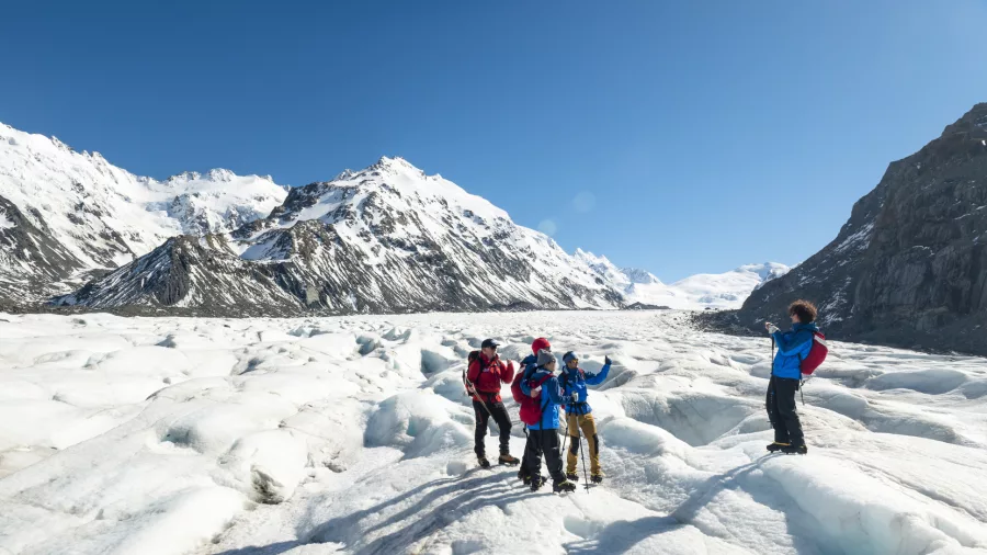 Group of hikers celebrating atop Tasman Glacier with snow-covered peaks all around.