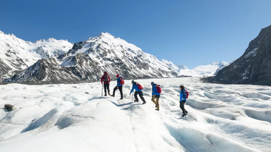 Group of hikers making their way across the Tasman Glacier with scenic mountains in the distance.