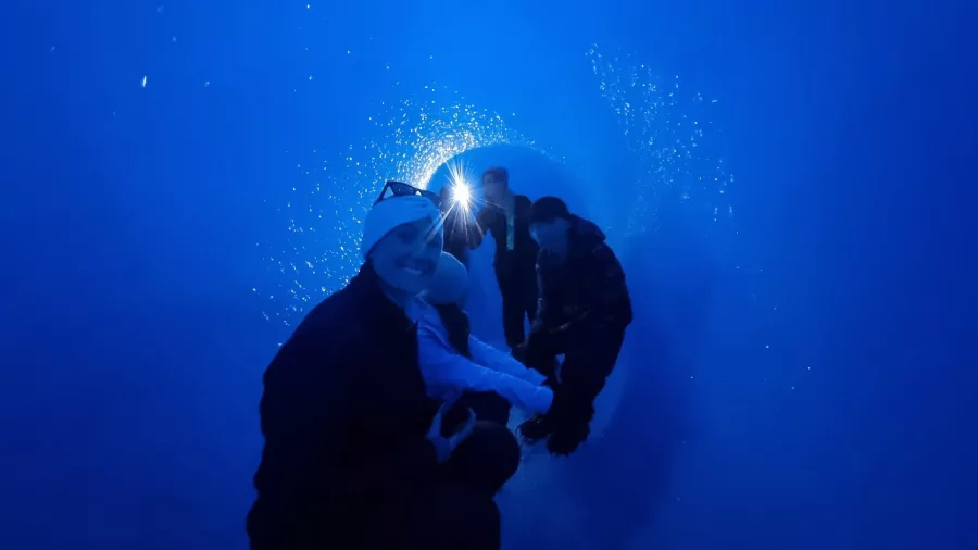 People inside a glowing deep-blue ice tunnel on the Tasman Glacier, New Zealand.