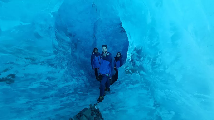 Hikers framed by glowing blue tunnel walls inside the Tasman Glacier.