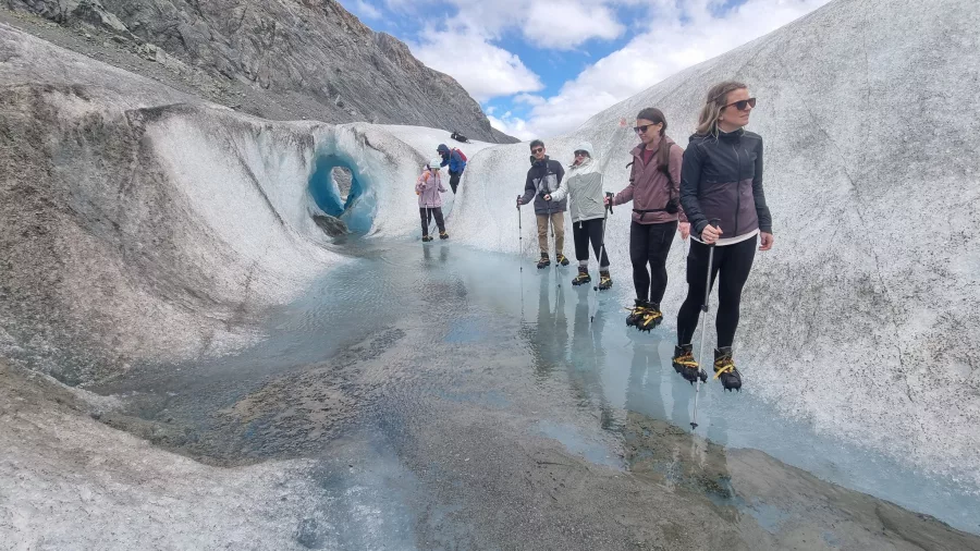 Group of hikers walking beside shimmering meltwater pools on Tasman Glacier.