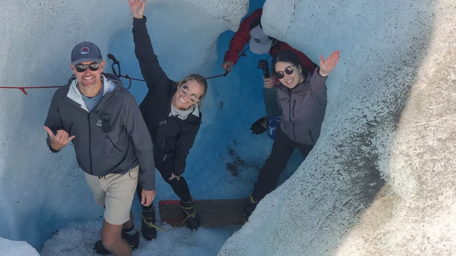 Happy hikers waving from inside a narrow ice tunnel on the Tasman Glacier.