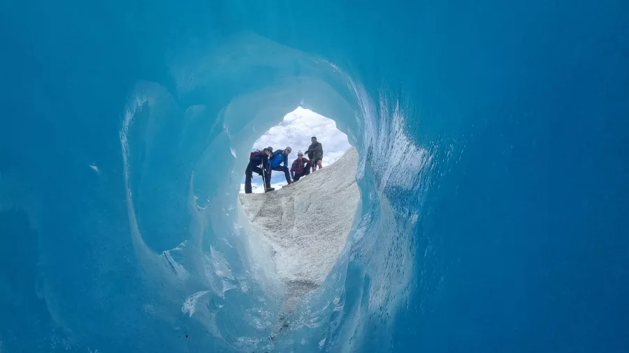 Group of hikers seen through the exit of a brilliant blue glacier cave.