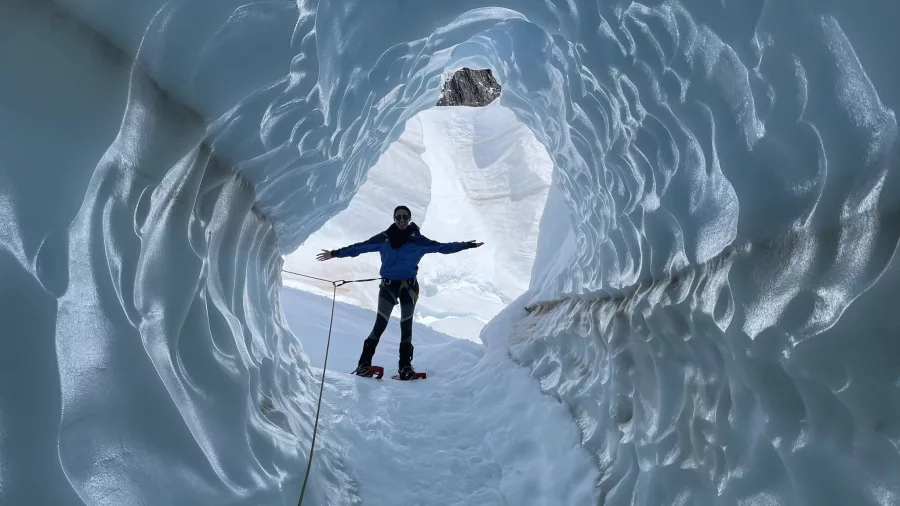 Solo hiker standing with arms open inside a sculpted glacier tunnel on Tasman Glacier.