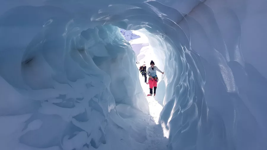 Hiker walking out of a glowing glacier tunnel during a heli hike on Tasman Glacier.