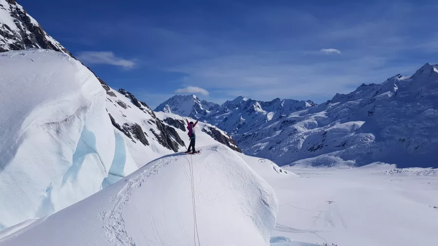 Hiker standing on a snow-covered ridge with expansive views of the Southern Alps.