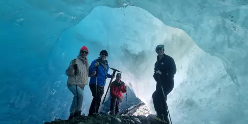 Group of hikers inside a glowing blue ice cave on the Tasman Glacier.