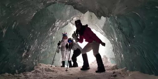 Hikers crouching through an icy tunnel on a guided heli hike on the Tasman Glacier.
