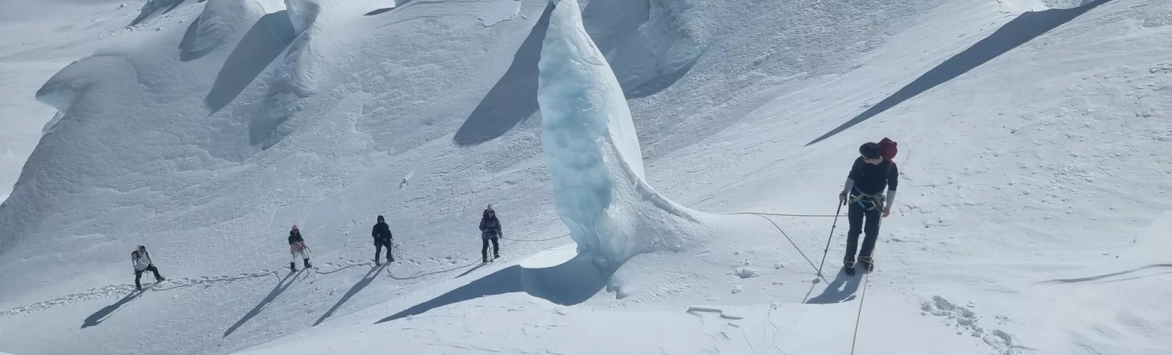 Group of snowshoers roped together navigating dramatic ice formations on Tasman Glacier.