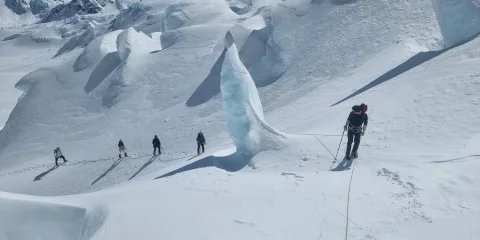 Group of snowshoers roped together navigating dramatic ice formations on Tasman Glacier.
