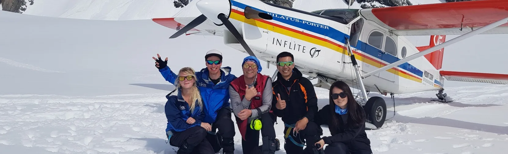 Group of happy passengers posing in front of ski plane after landing on snow near Mount Cook