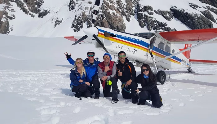 Group of happy passengers posing in front of ski plane after landing on snow near Mount Cook