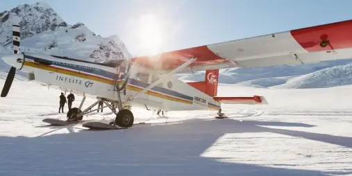 Inflite ski plane on a snowy landing site near Mount Cook with sunburst over the mountains