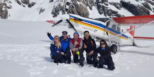 Group of happy passengers posing in front of ski plane after landing on snow near Mount Cook