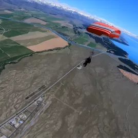 Tandem skydivers descending with red parachute over Lake Pukaki and Canterbury Plains
