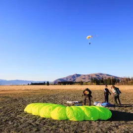 Bright green parachute on the ground with skydivers approaching landing zone near Mount Cook