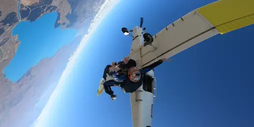 Skydivers launching from plane with Lake Tekapo visible far below