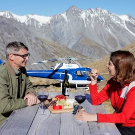Couple enjoying a private alpine picnic beside a helicopter with mountain views in the Mackenzie Region