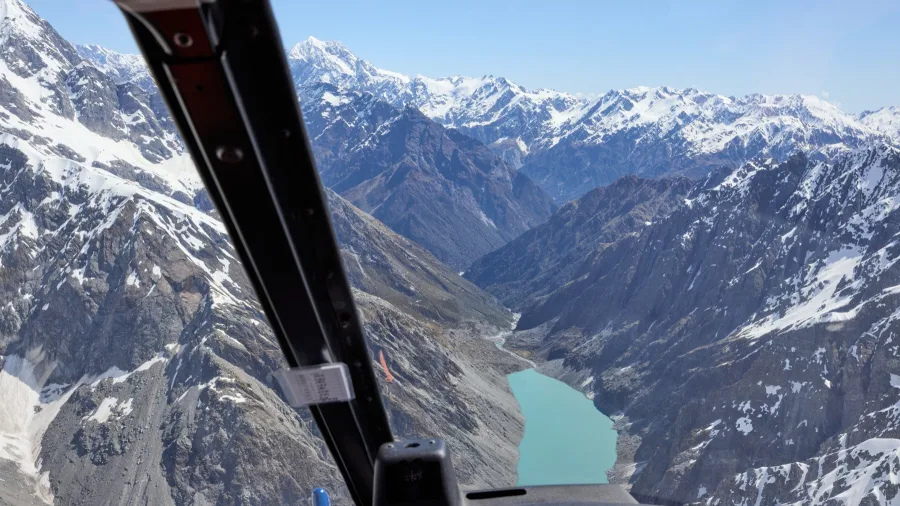 Cockpit view of helicopter flying over Tasman Valley with glacial lake and snow-covered mountains