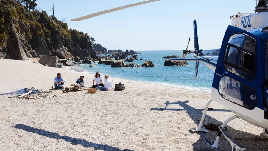 Helicopter parked on the sand as guests enjoy a beach picnic beside the turquoise sea