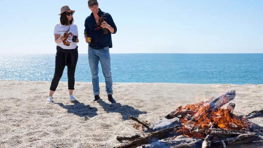 Couple cooking crayfish over a beach bonfire beside the sea during a luxury helicopter tour