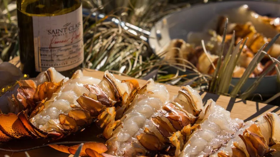 Close-up of fresh crayfish tails and a bottle of Saint Clair wine on a beach platter