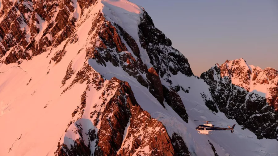 Helicopter flying past Mount Sefton at sunset with alpenglow lighting up the peaks