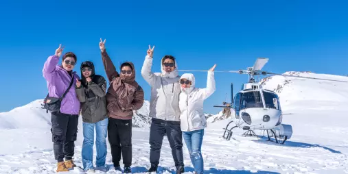 Group posing on snow-covered mountain after helicopter landing near Lake Tekapo