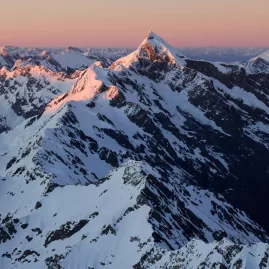 Sunset light hitting snow-covered Southern Alps peaks during a scenic flight