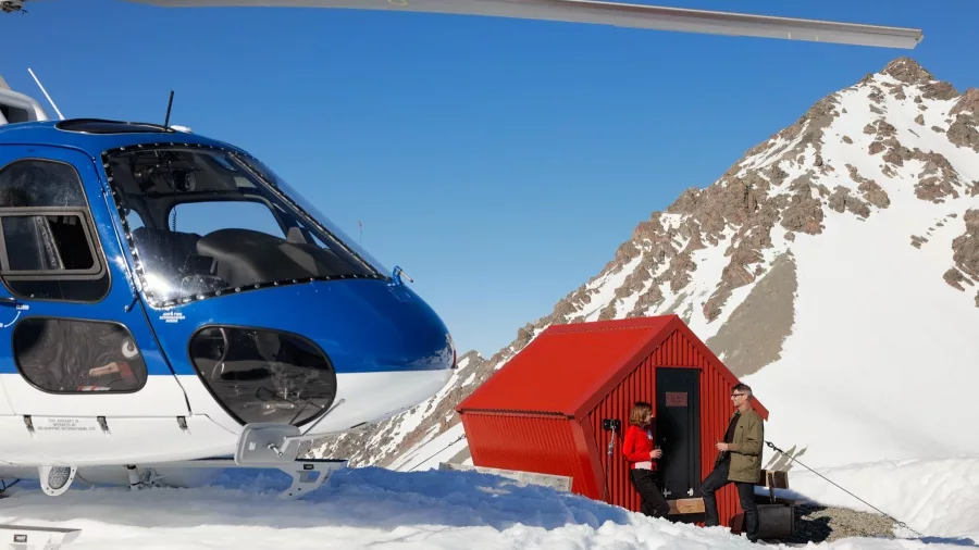 Helicopter parked beside red whisky hut high in the Southern Alps of New Zealand